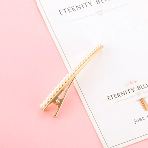 Elegant gold hair clip featuring white pearls on a pink and white minimalist backdrop
