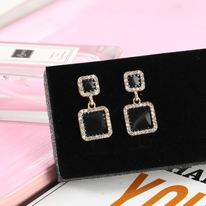 Elegant black enamel square drop earrings with sparkling crystals on a pink display