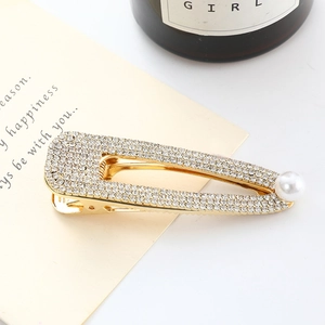 Détail d'une barrette dorée ornée de strass brillants et d'une perle blanche élégante