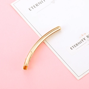 Elegant gold metal hair clip with polished finish on a minimalist pink background