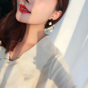 Close-up of minimalist black and gold geometric earrings worn with side natural lighting
