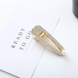 Détail d'une barrette dorée ornée de strass et d'une perle sur une carte de support