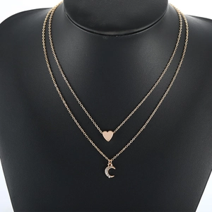 Layered gold heart and crescent moon pendant necklace on a black mannequin display