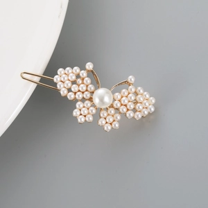 Detail view of a golden butterfly hair clip with white pearls on a grey background