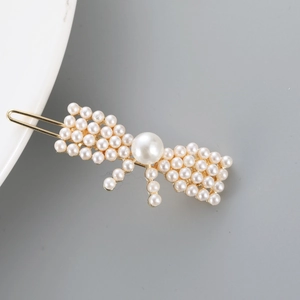 Detailed view of elegant gold-toned hair clip with white faux pearls in a bow shape