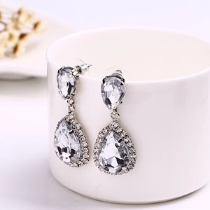 Detailed close-up of teardrop zircon earrings hanging on a white porcelain cup edge