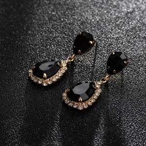 Detail of tear-drop earrings featuring black faceted stones and gold metal plating