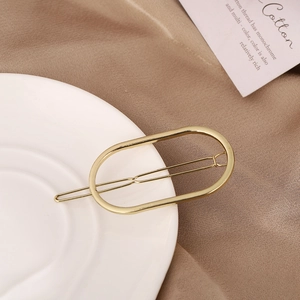 Vista detallada de un elegante pasador de pelo ovalado dorado sobre un plato blanco