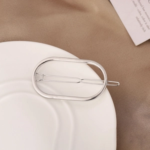 Detalle de pinza para el cabello geométrica ovalada plateada en plato de cerámica blanca