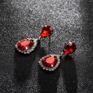 Close-up of sparkling red pear-cut zircon drop earrings with silver-toned halo settings