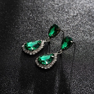 Macro view of teardrop emerald earrings with sparkling white zircon halo on dark background