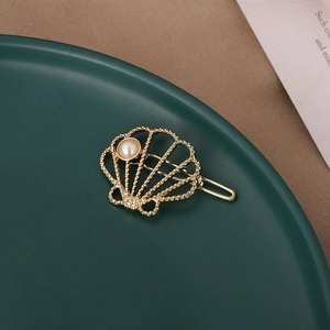 Fermaglio dorato a conchiglia con perla bianca su sfondo verde vintage raffinato