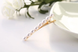 Gros plan détaillé d'une barrette en métal doré avec huit perles rondes blanches