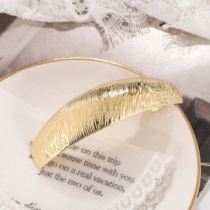 Elegant gold curved spring hair clip with a brushed texture on a white lace background