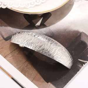 Silver metallic hair clip with textured matte finish on an elegant magazine background