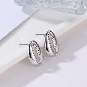 Macro shot of polished silver shell stud earrings with detailed serrated edges on a white stand