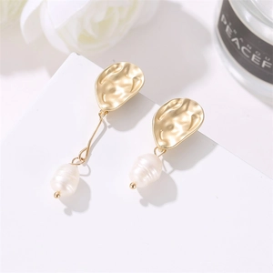 Detailed view of asymmetric gold-tone drop earrings with freshwater pearls on white floral set
