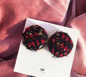 Detail of red and black tweed plaid round stud earrings on a pink velvet background