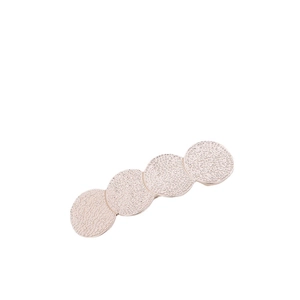 Détail macro d'une pince à cheveux géométrique or rose avec quatre disques ronds