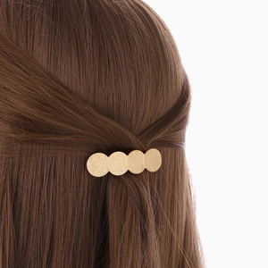 Barrette dorée mate minimaliste avec quatre disques géométriques sur cheveux bruns