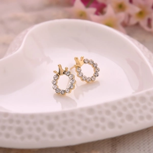 Macro shot of gold-plated crown earrings with white rhinestones on a ceramic tray