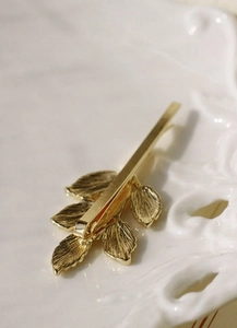 Détail d'une pince à cheveux branche d'olivier dorée avec texture de feuilles fine