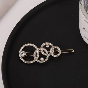Barrette dorée élégante avec anneaux évidés, perles et strass sur plateau noir mat