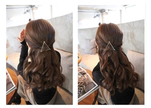 Minimalist gold triangle metal hair clip worn on long brown hair in a cozy cafe setting