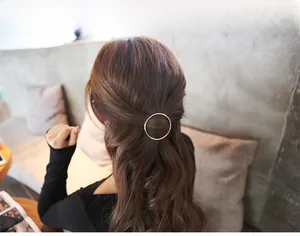 Minimalist gold metal round hair clip shown on model with long wavy dark brown hair