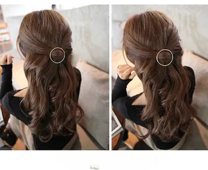 Detail view of a minimalist round gold metal hair clip styled on wavy brown hair