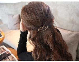 Lip-shaped hollow metal hair clip in gold finish worn on wavy hair in a cozy setting