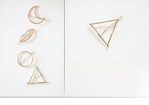 Detailed close-up of minimalist gold-plated geometric hair clips in moon and triangle shapes