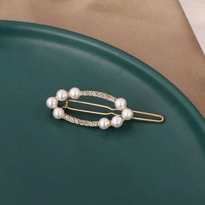 Eleganter ovaler Goldhaarsclip mit weißen Perlen und glitzernden Strasssteinen auf Tablett