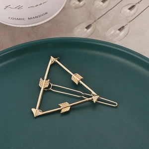 Détail macro d'une barrette géométrique dorée en forme de triangle avec des motifs fléchés