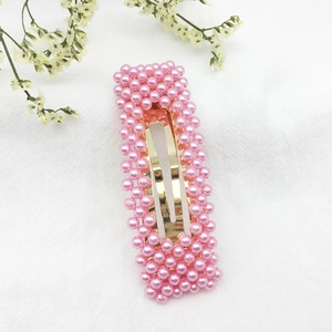 Dettaglio della molletta con perle rosa e base in metallo dorato su tessuto bianco