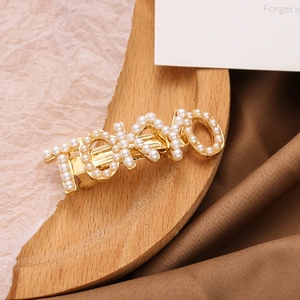 Eleganter goldener TOKYO Buchstaben-Haarclip mit weißen Perlen auf Holztablett