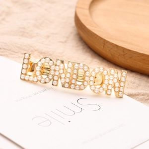 Pince à cheveux dorée avec lettres LONDON et perles blanches sur un plateau en bois