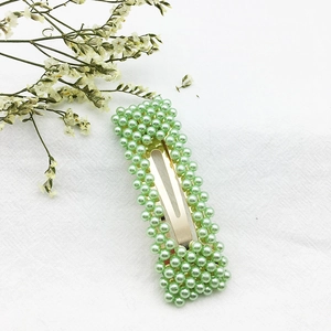Dettaglio di un fermaglio per capelli in metallo dorato con perle verde chiaro su fondo bianco