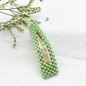 Dettaglio di un fermaglio dorato con perle artificiali verde chiaro su tessuto bianco