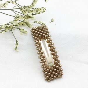 Dettaglio di un fermaglio BB dorato rettangolare con perle marroni su lino bianco