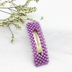 Dettaglio ravvicinato di un fermaglio dorato con perle viola su tessuto bianco