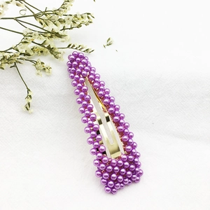 Dettaglio di fermaglio per capelli con perle viola e base dorata su tessuto bianco