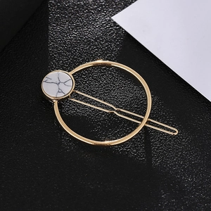 Minimalist gold hair clip with white marble stone detail on a sleek black background