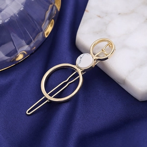 Minimalist gold metal hair clip with white marble inlay on blue silk background