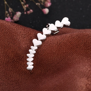 Elegant silver heart-shaped ear cuff for women on brown textured fabric with flowers