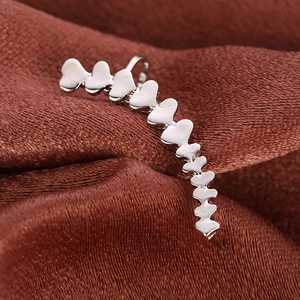 Polished silver heart-shaped alloy ear cuff earrings on brown satin fabric background