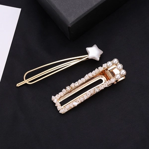 Golden hair clip set with white star and pearl-encrusted rectangle pin on black surface