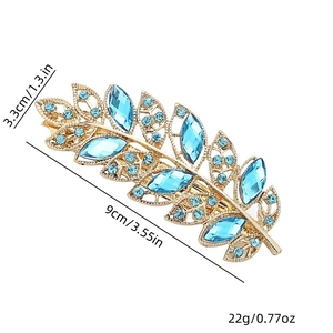 Detail view of leaf-shaped gold hair clip with blue crystals and 9cm size measurement