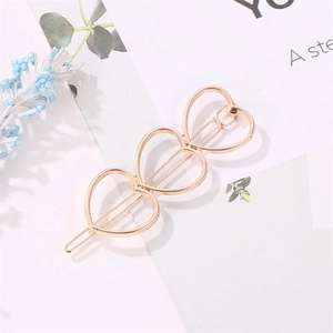 Detail of three hollow heart-shaped metal hair clips in pale gold finish on floral card