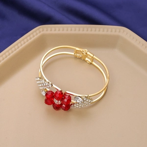 Detail view of gold floral bracelet with red crystals on a blue velvet background